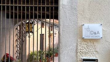 Una entrada vigilada con un letrero de número, un cartel de villa y un intercomunicador de seguridad.