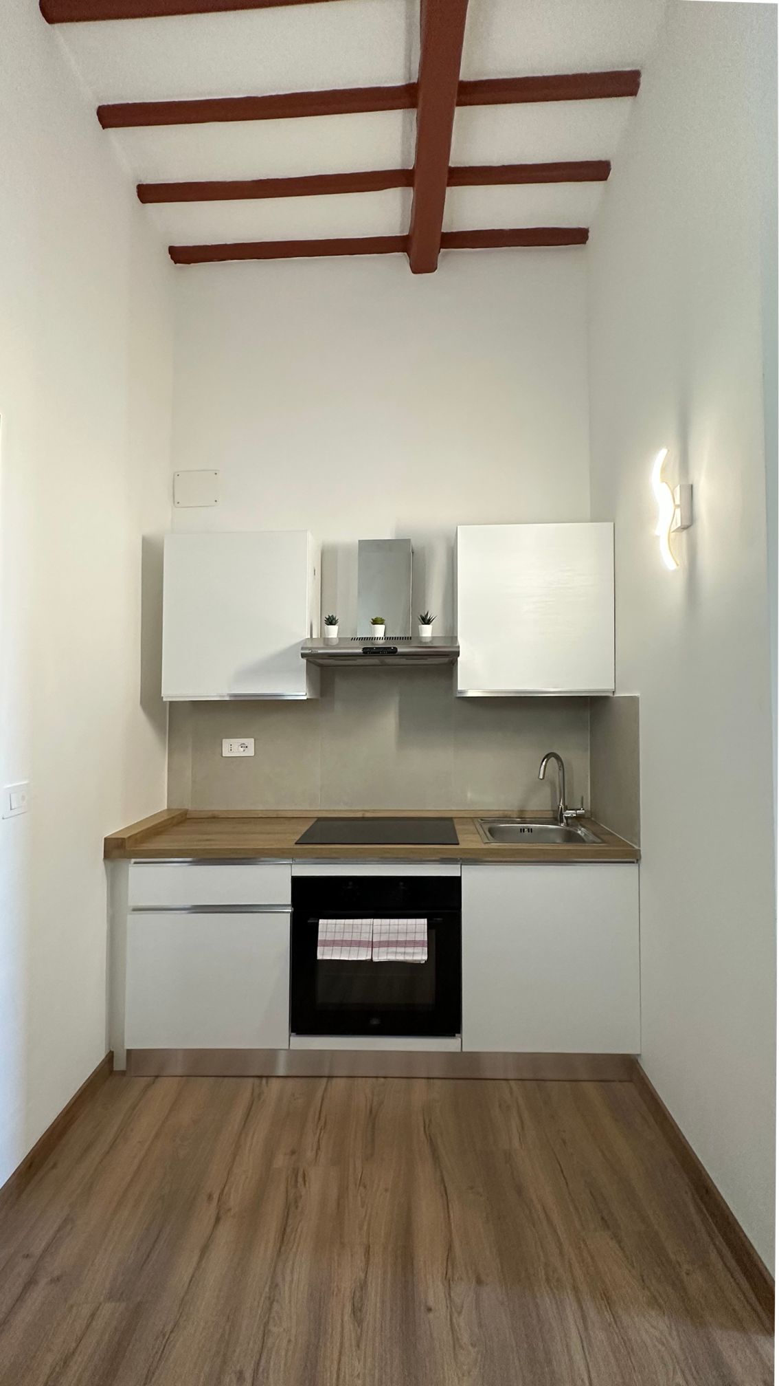 Una cocina compacta con armarios blancos, encimera de madera y horno empotrado.
