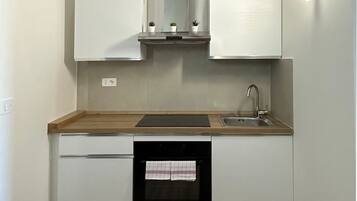 Una cocina compacta con armarios blancos, encimera de madera y horno empotrado.