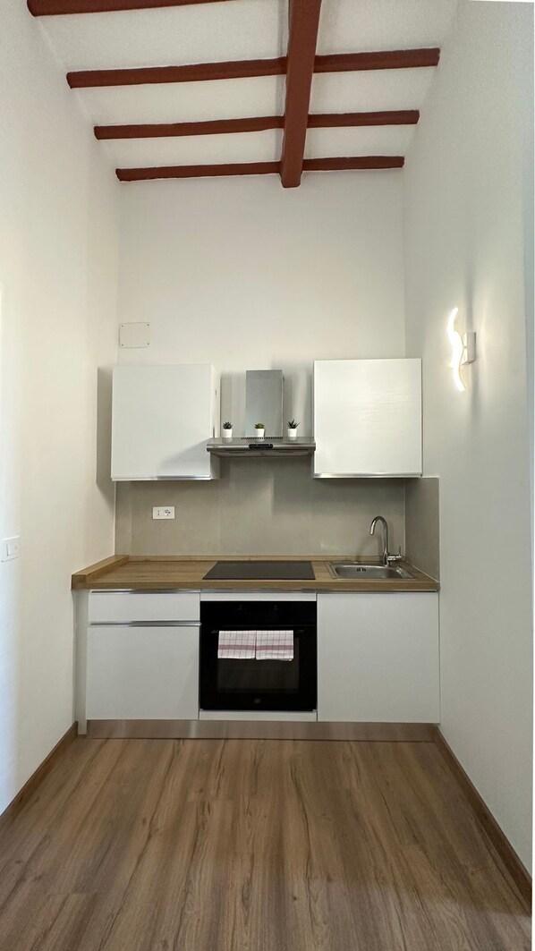 A compact kitchen with white cabinets, a wooden countertop, and a built-in oven. - New Listing (Orvieto)