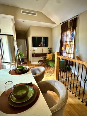 Une cuisine moderne avec un coin repas, un téléviseur à écran plat fixé au mur et un escalier doté d’une rampe.