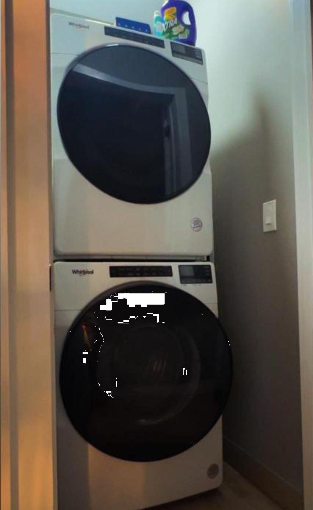 Un appareil combiné lave-linge et sèche-linge, avec un panneau de commande et un flacon de lessive placés sur le dessus.