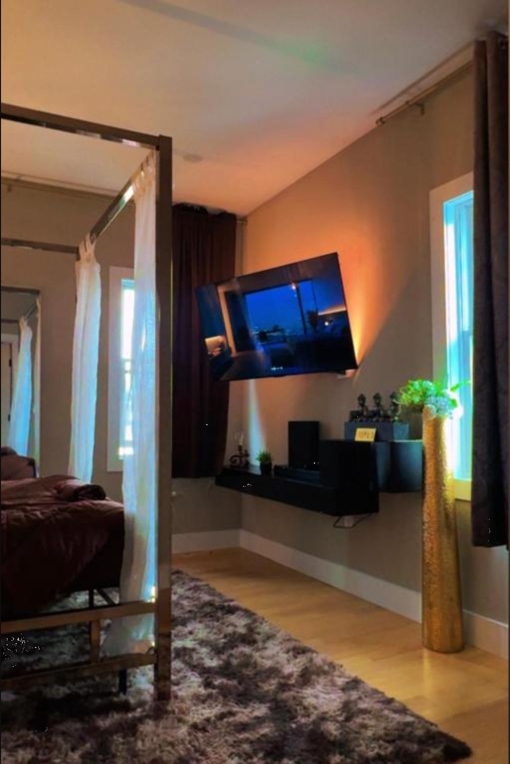 Un salon moderne avec un téléviseur à écran plat fixé au mur, un canapé de couleur foncée, une table basse en bois et une grande plante en pot.