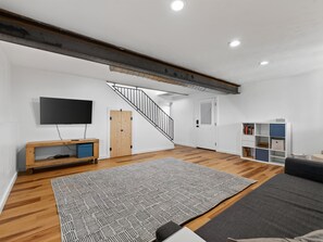 A modern living room with a wooden floor, a large rug, a flat-screen TV, a bookshelf, and a staircase. - NEW! Ridges Retreat III w/Mountain Views (Grand Junction)