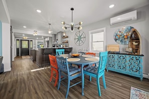 A modern kitchen with a dining area, featuring a central island, pendant lighting, and a decorative wall piece. - Renovated Lakefront Home- Deck, Grill and Views (Seneca Falls)