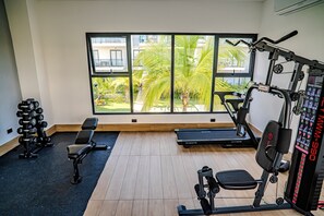 A gym with exercise equipment, a treadmill, and a view of a building and trees through large windows. - New Listing (Punta Cana)