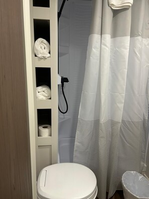 Un bagno con il water, uno scaffale con asciugamani, una tenda per la doccia e un rotolo di carta igienica.