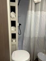 Et badeværelse med toilet, hylder med håndklæder, bruseforhæng og toiletpapir.