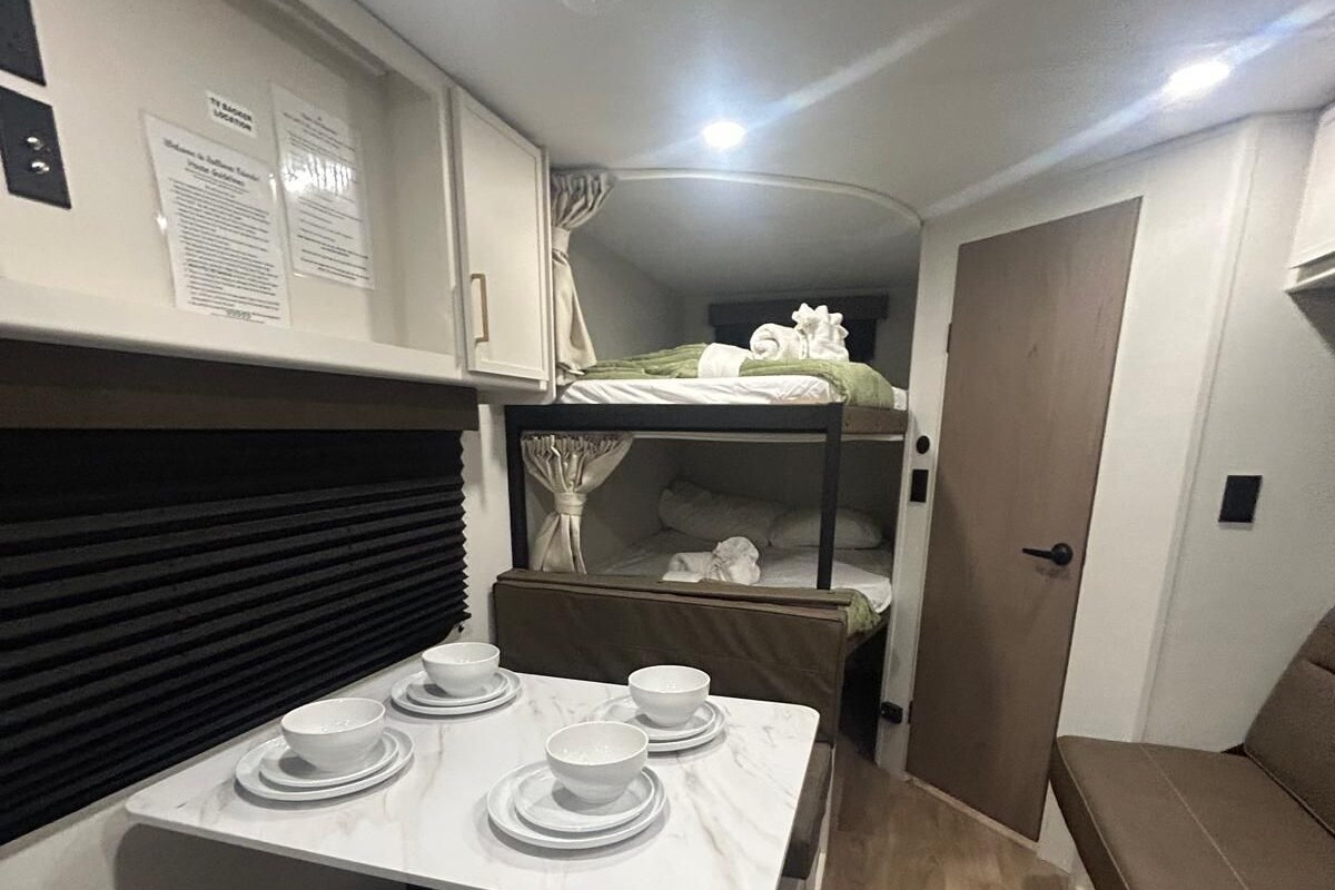 Un angolo cottura compatto con un tavolo apparecchiato per mangiare, un letto a castello e una porta che dà su un'altra stanza.