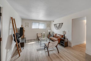 A spacious living room with a wooden floor, a glass coffee table, a leather sofa, and a dining area with a chair and table. - Prime Location! HGTV Design! (Omaha)