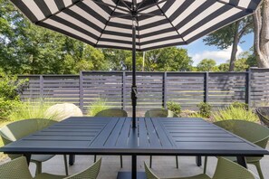 Eine Terrassengaststätte mit Tisch und Stühlen, einem gestreiften Sonnenschirm und einem Holzzaun im Hintergrund.