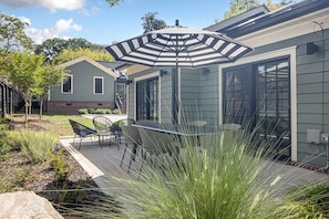 A patio with a table and chairs, a striped umbrella, and a brick house in the background. - The Wilmore Cottage by South End | King Bed, Skylights, Fireplace & Private Patios (Charlotte)