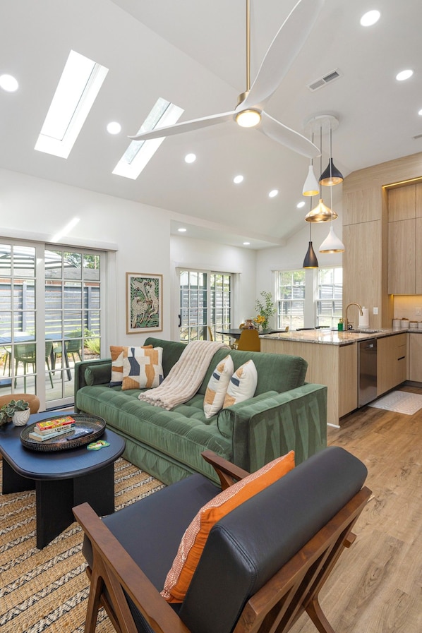 Una sala moderna con un sofá verde, una mesa de centro y un comedor con una cocina al fondo.