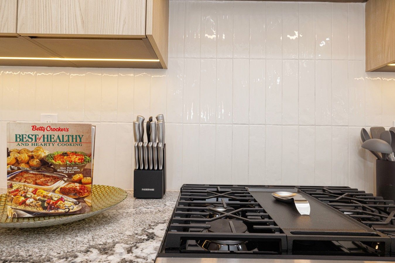A kitchen with a gas stove, a knife block, and a cookbook titled 'Betty Crocker's Best of Healthy and Hearty Cooking'.