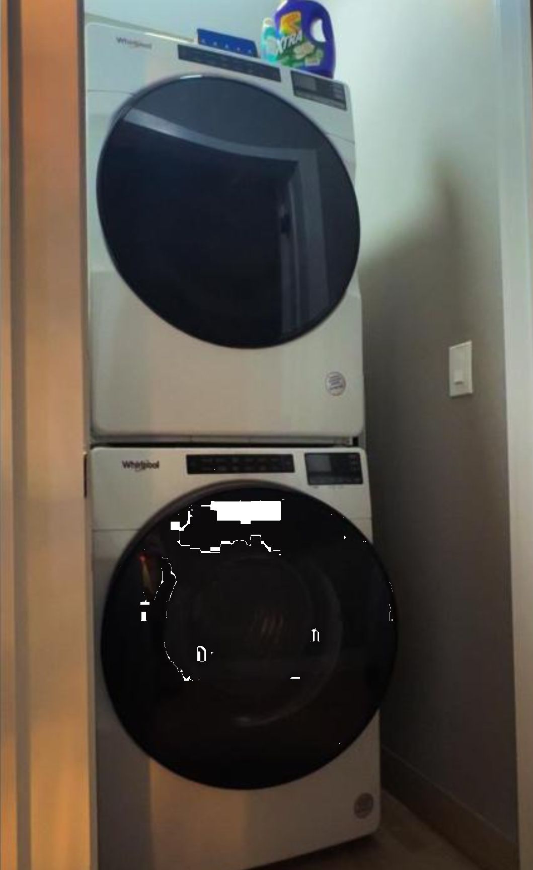 Un appareil combiné lave-linge et sèche-linge, avec un bidon de lessive placé sur le dessus.