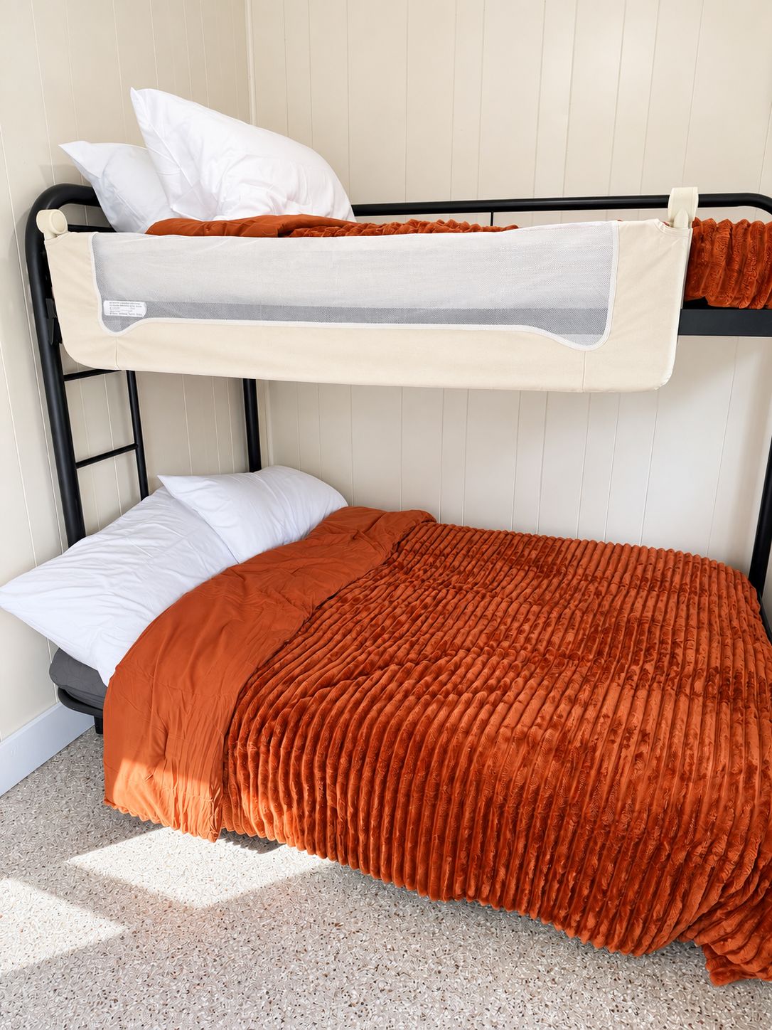 A bunk bed with a mattress and pillows, a grey headboard, and a beige wall.