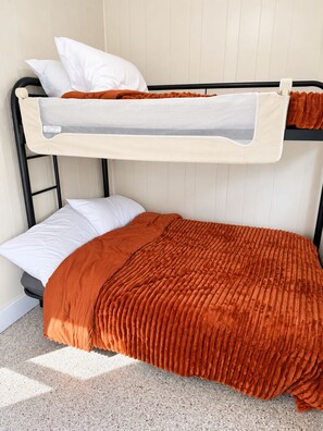 Una cama litera con colchón y almohadas, un cabecero gris y una pared beige.