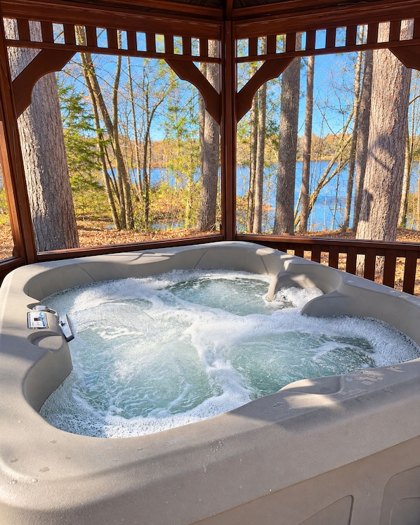 A hot tub with a wooden pergola structure, surrounded by trees and a body of water.