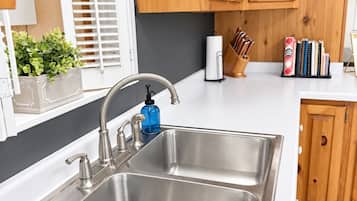 Una cocina con un lavamanos de acero inoxidable, armarios de madera, una ventana con persianas y una planta en maceta.