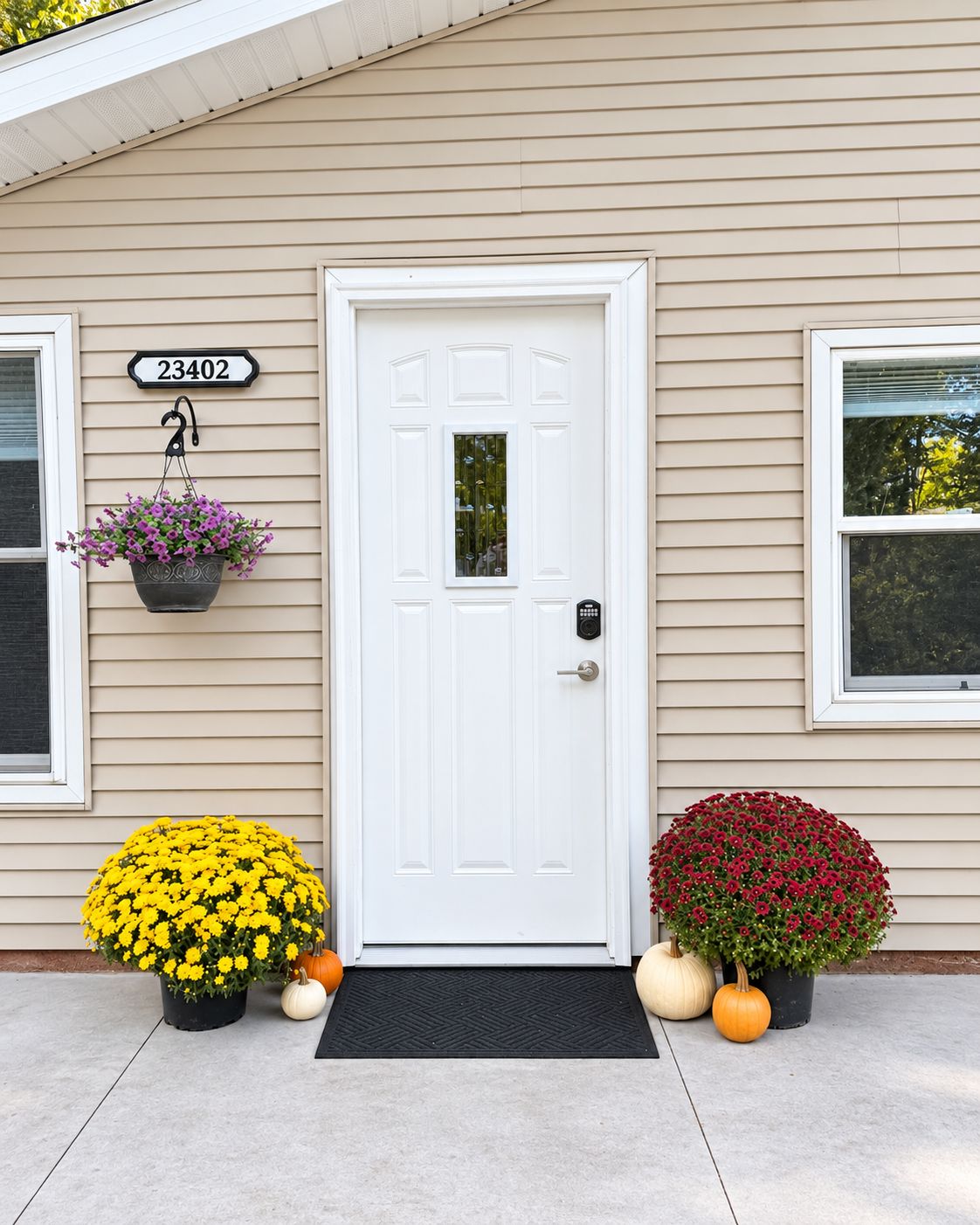 A house with a white door, number 23402, a black mailbox, and two flower pots with yellow and red flowers.