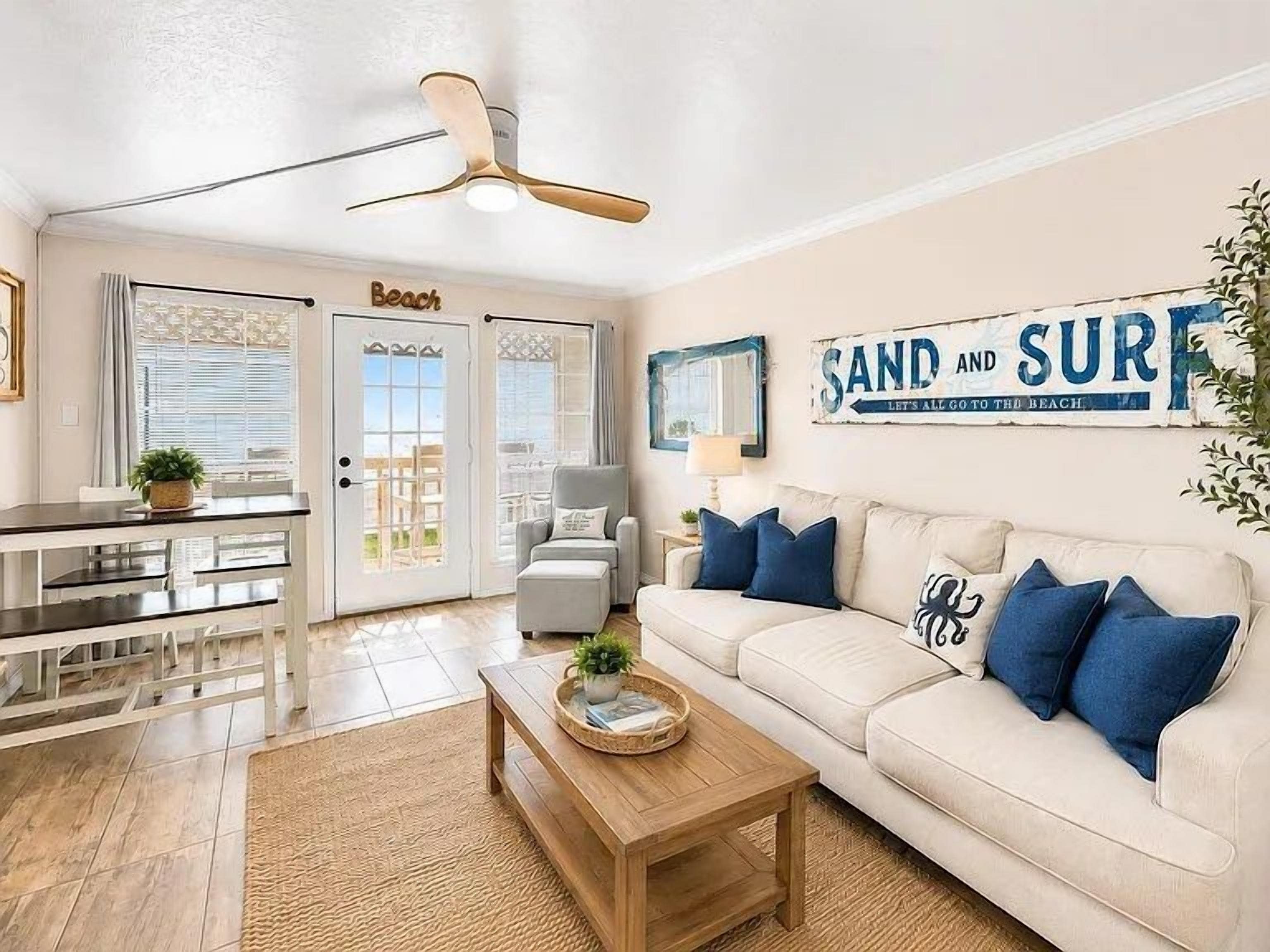 A living room with a white sofa, blue cushions, a wooden coffee table, and a ceiling fan.