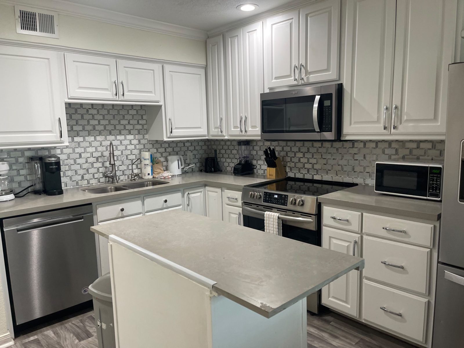 Una cocina moderna con muebles blancos, electrodomésticos de acero inoxidable y un salpicadero de azulejos.
