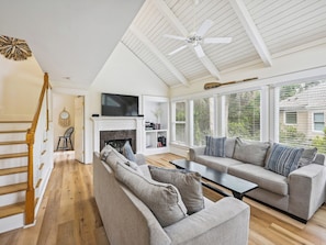 A spacious living room with a fireplace, a ceiling fan, and a large window with blinds. - Tropical Oasis Steps From The Shoreline w/ Pool! (Hilton Head Island)
