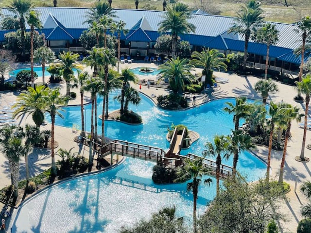 A resort with multiple swimming pools, palm trees, and a bridge connecting different areas.