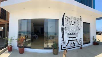 A modern building with large glass doors and windows, a mural on the exterior wall, and potted plants outside.