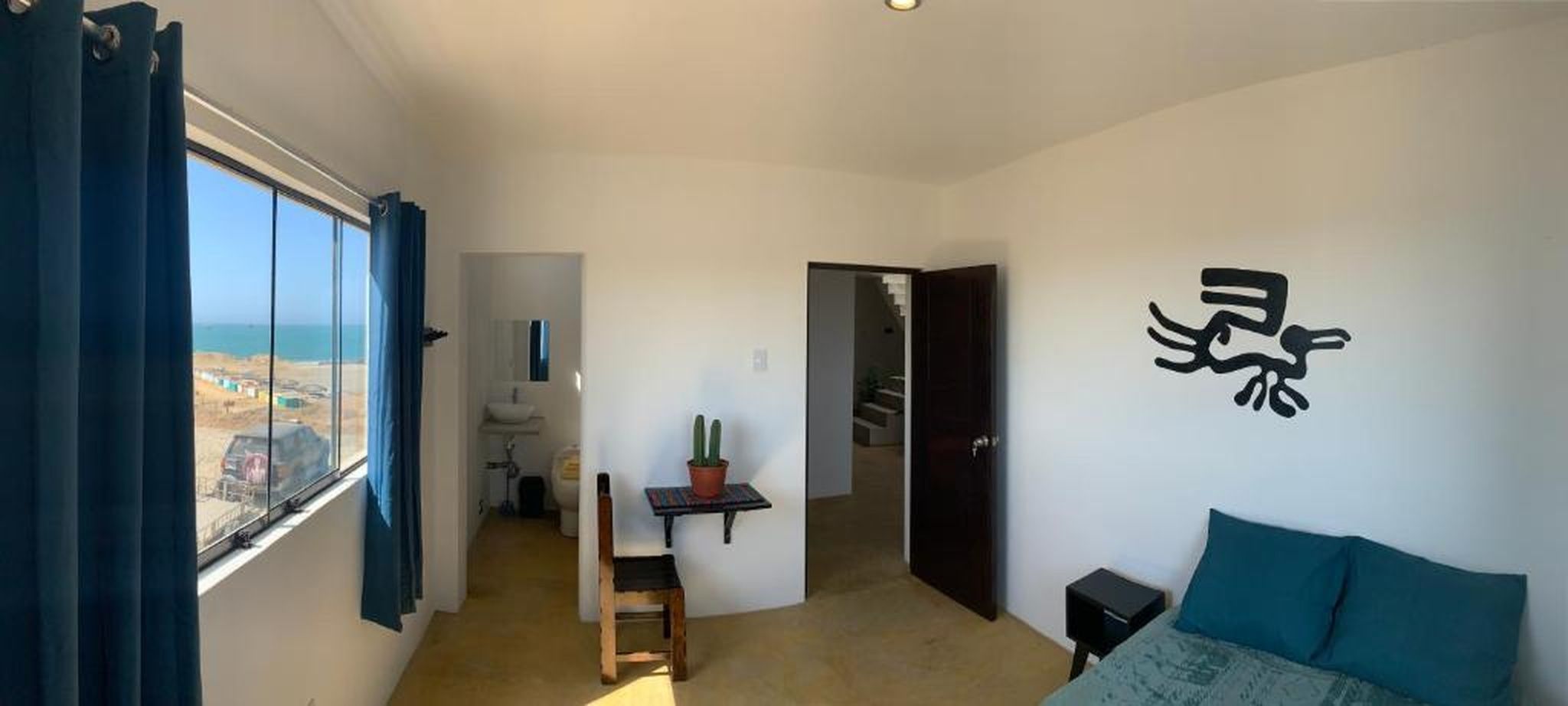 Una habitación con una cama, un escritorio, una silla, un ventanal con cortinas y una pared con un diseño abstracto en tonos negros.