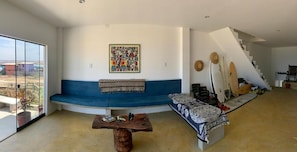 A living room with a blue sofa, a wooden coffee table, a colorful abstract painting, and a staircase with surfboards.