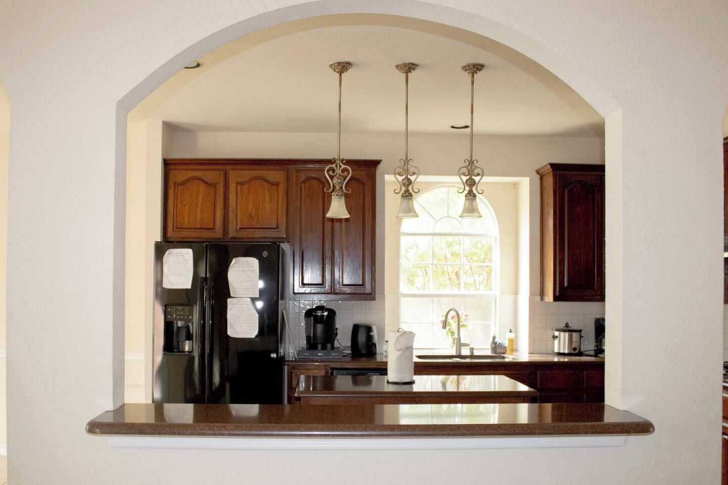A kitchen with wooden cabinets, a black refrigerator, a coffee maker, and pendant lights.