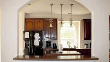 A kitchen with wooden cabinets, a black refrigerator, a coffee maker, and pendant lights.