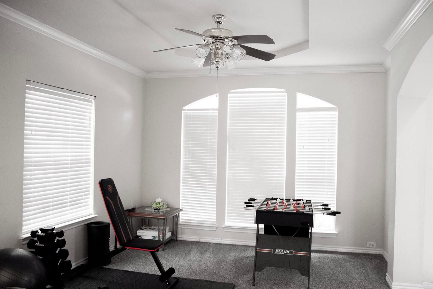 A room with a ceiling fan, a foosball table, a chair, and exercise equipment.