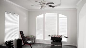 A room with a ceiling fan, a foosball table, a chair, and exercise equipment.