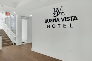 Interior de un hotel con una escalera, un letrero de salida y una pared con el nombre del hotel.