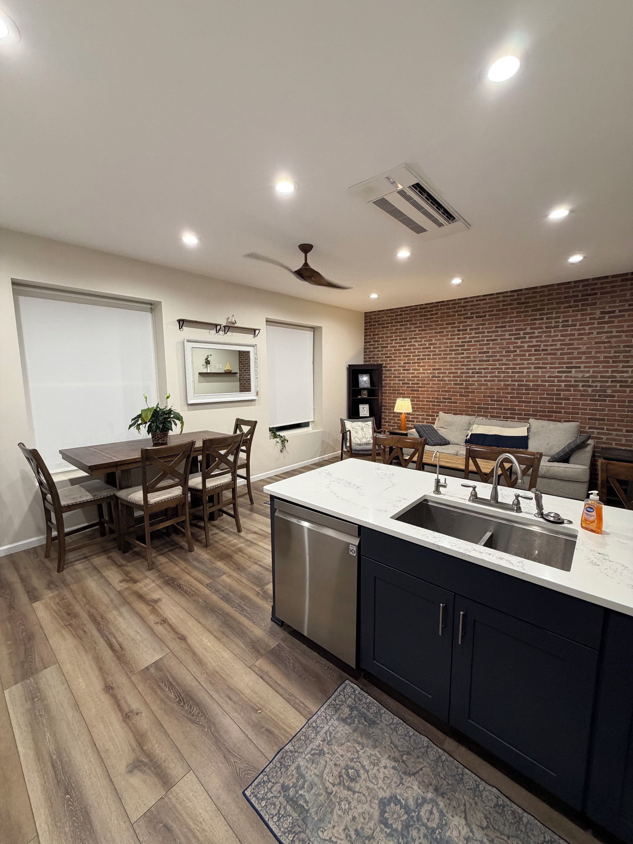 A modern kitchen with a central island, built-in dishwasher, and a brick accent wall.