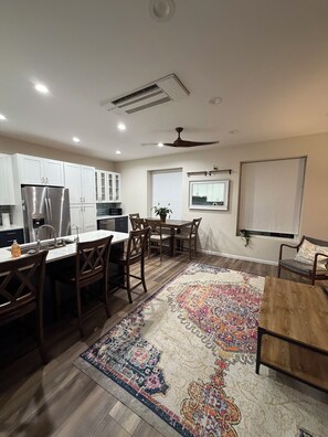 A modern kitchen with white cabinetry, a stainless steel refrigerator, a dining area with a wooden table and chairs, and a patterned rug on the floor. - Perfect 3-bedroom apartment in the heart of Port Clinton (Port Clinton)