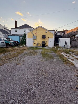 A gravel driveway leading to a yellow building with a covered outdoor area, a stairway, and a fenced yard. - Perfect 3-bedroom apartment in the heart of Port Clinton (Port Clinton)