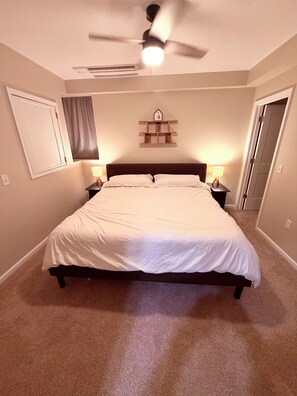 A bedroom with a bed, two bedside lamps, a ceiling fan, a wall-mounted shelf, and a door. - Perfect 3-bedroom apartment in the heart of Port Clinton (Port Clinton)