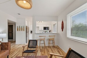 Ein modernes Wohnzimmer mit Holzboden, einem braunen Ledersofa, einer Essecke mit drei Holzstühlen und einer Küche im Hintergrund.