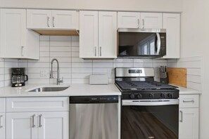 Une cuisine moderne avec des meubles blancs, une cuisinière en acier inoxydable, un four à micro-ondes et un lave-vaisselle.