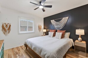 Een slaapkamer met een bed, nachtkastjes, een plafondventilator, een raam met jaloezieën en wanddecoratie.