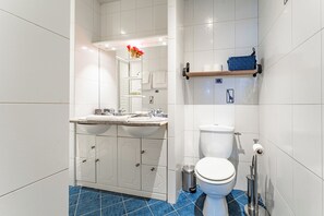 A modern bathroom with a double sink, toilet, and a blue-tiled floor. - New Listing (Bordeaux)