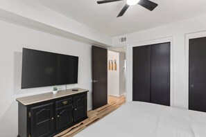 Ein Schlafzimmer mit einem Bett, einem an der Wand montierten Fernseher, einem dunklen Holzschrank und einem Deckenventilator.