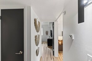 A hallway with a dark door, a light-colored wall, and a wooden floor. - Cozy Stylish Apt in Omaha`s Medical District! (Omaha)