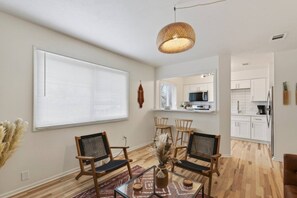 A modern living room with a dining area, a kitchen in the background, and a large window with blinds. - Cozy Stylish Apt in Omaha`s Medical District! (Omaha)