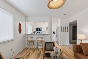 A modern living room with a wooden floor, a brown sofa, and a dining area with two wooden chairs. - Cozy Stylish Apt in Omaha`s Medical District! (Omaha)