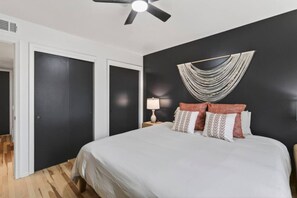 A bedroom with a bed, a ceiling fan, a wall-mounted lamp, and a patterned wall decoration. - Cozy Stylish Apt in Omaha`s Medical District! (Omaha)