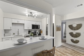 A modern kitchen with white cabinetry, a central island, and a dining area with a wooden chair. - Cozy Stylish Apt in Omaha`s Medical District! (Omaha)